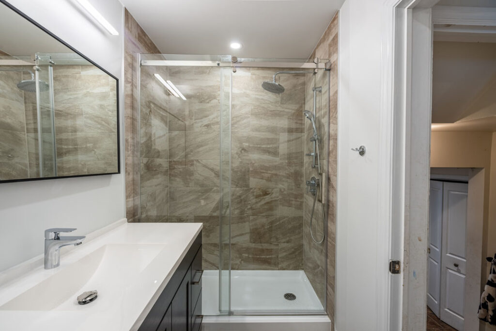 vanity with mirror and large tiled shower wall with rain effect shower head